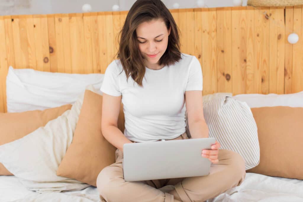 Female student sitting on her bed with laptop.